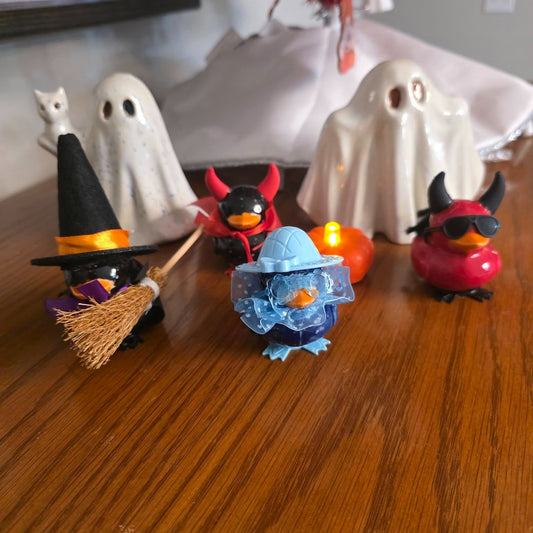 Four costumed duck figurines with witch, devil, and blue-hat outfits, displayed with two white ceramic ghosts.