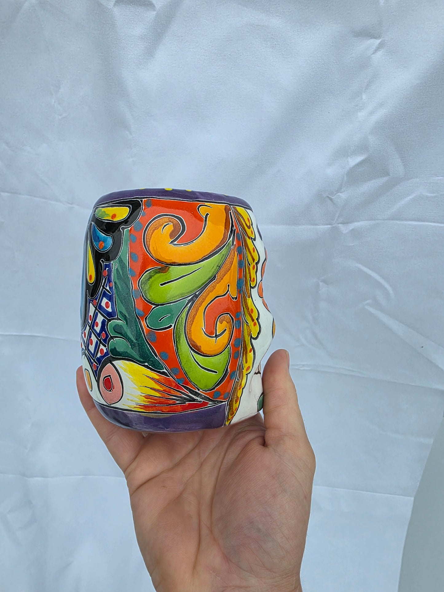 Colorful ceramic container held by a hand on a white background
