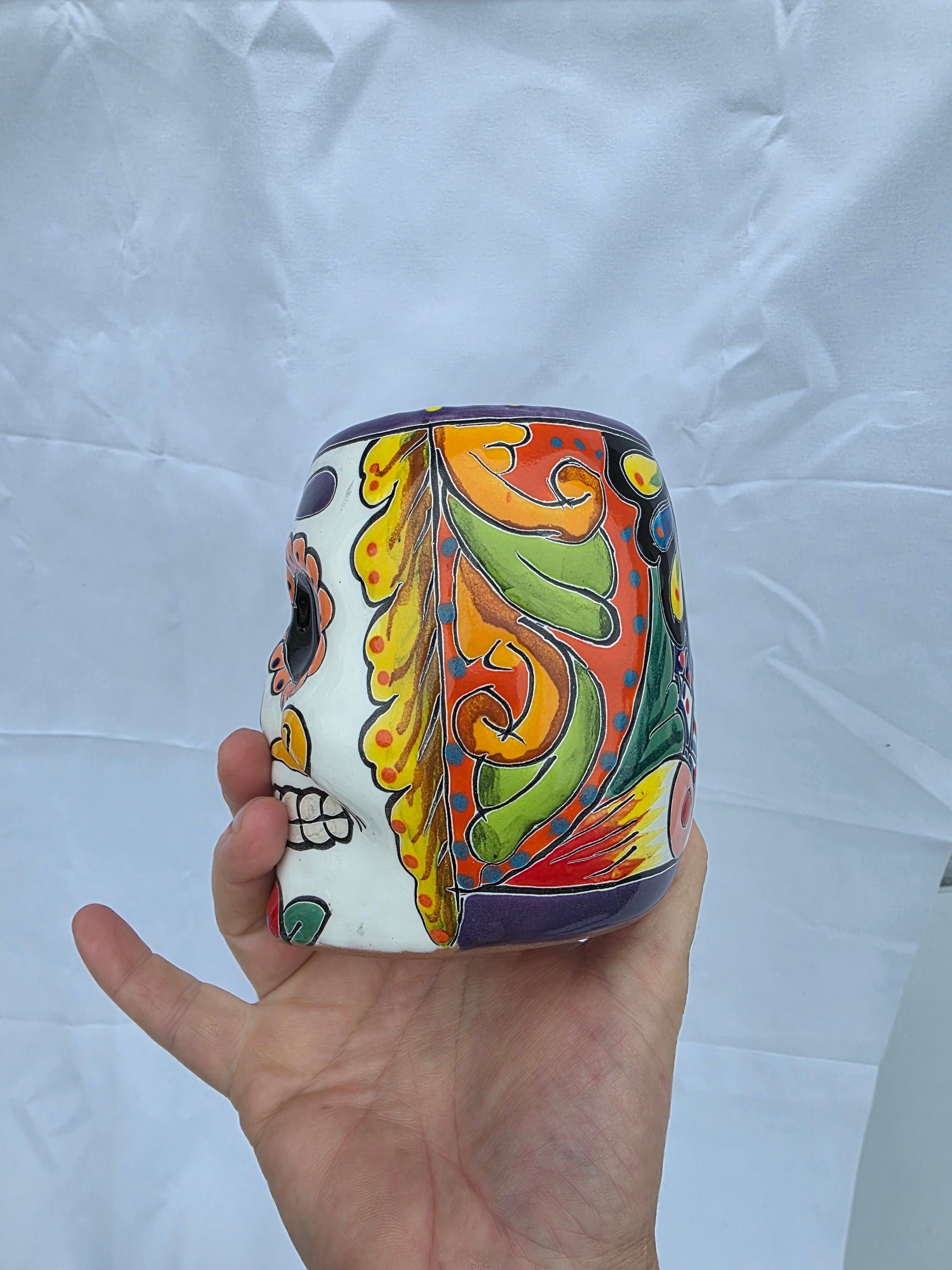 Colorful ceramic container held by a hand on a white background