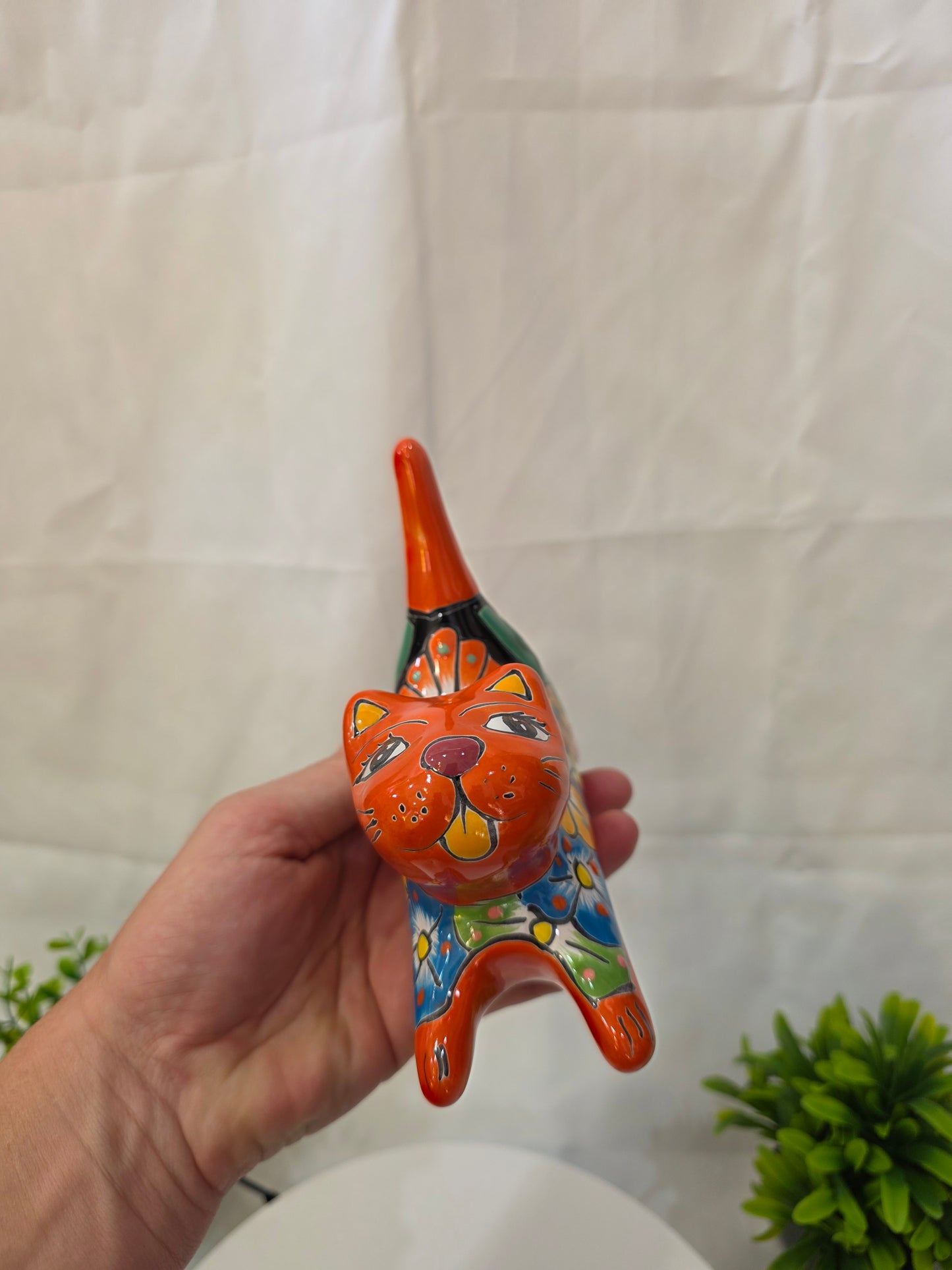 Hand holding a colorful ceramic CAT object against a light background