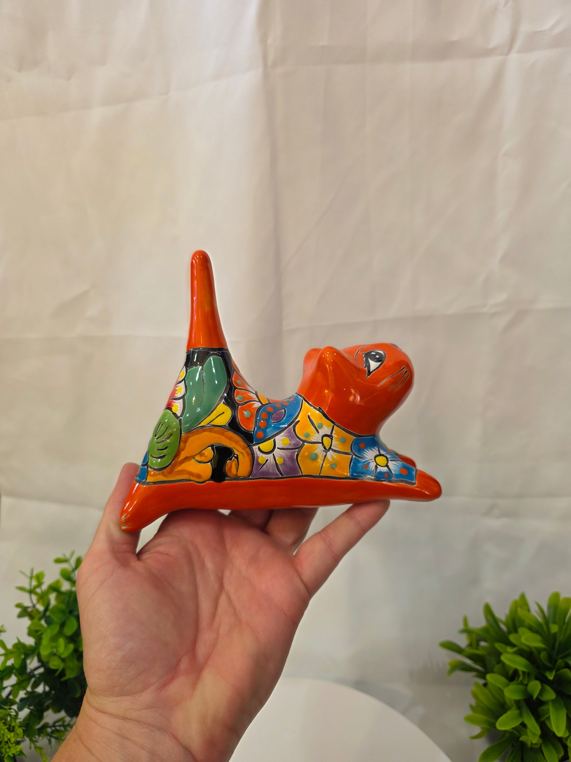 Colorful ceramic CAT figurine held in a hand against a plain background