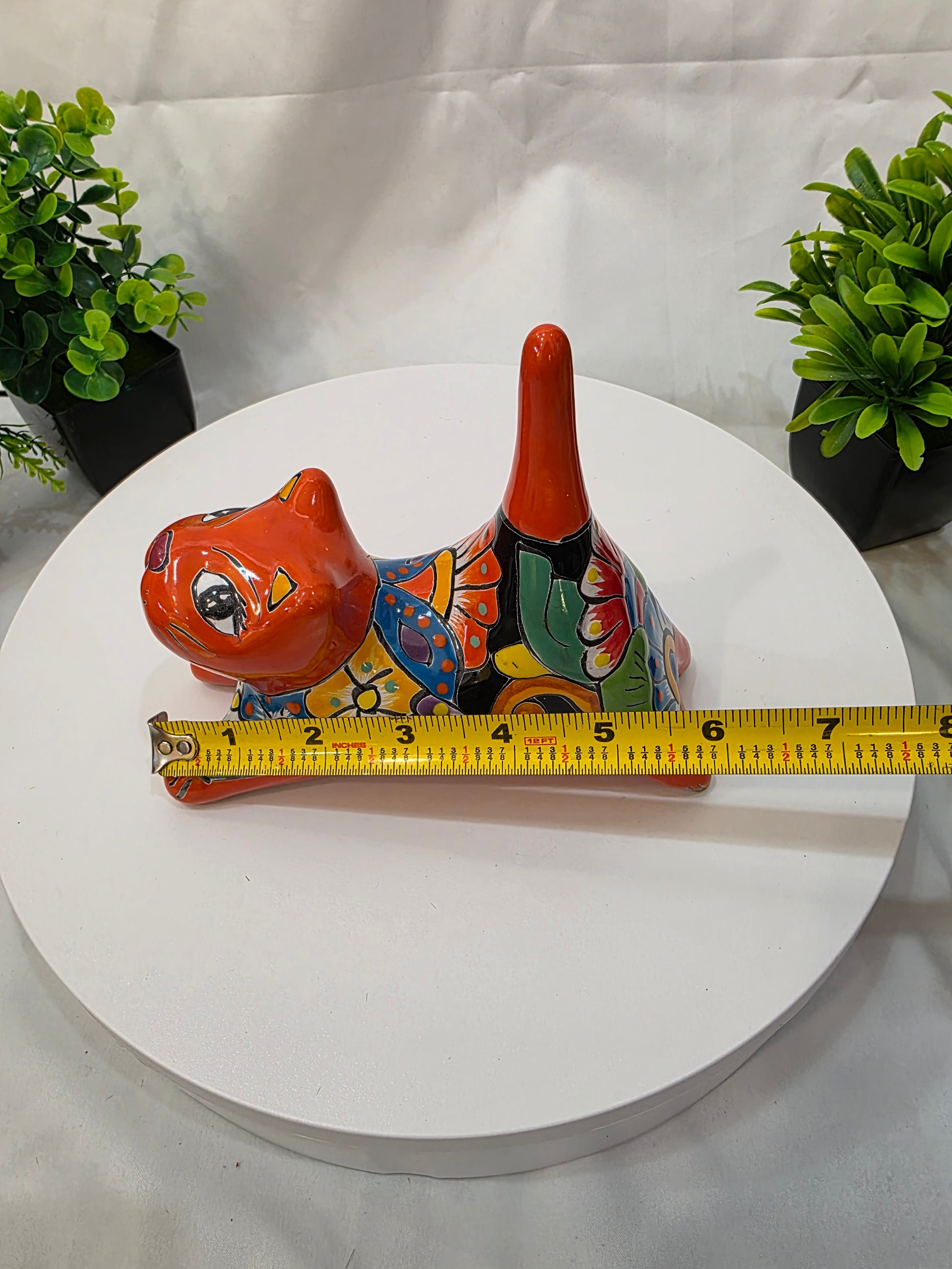 Decorative cat  with a measuring tape on a white surface with plants.
