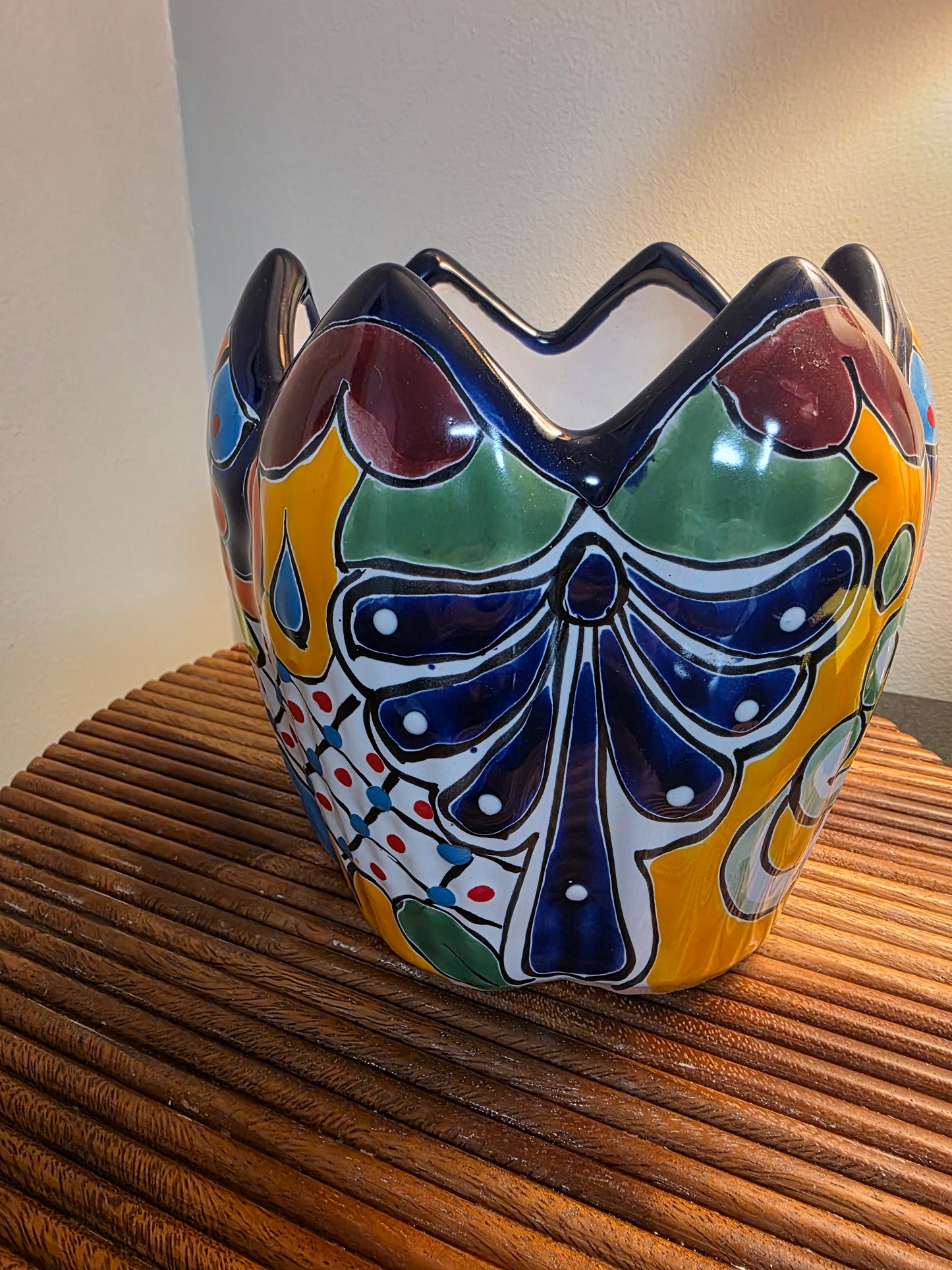 A colorful ceramic  planter with a hand-painted Mexican Talavera style design, featuring blue, green, yellow, and red patterns, shown mounted on a wooden slatted wall.