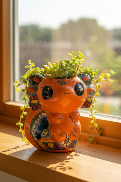 A hand holding a small, hand-painted ceramic cat figurine with a bright orange body and colorful, patterned details on its ears, back, and paws, set against a wrinkled white fabric background.