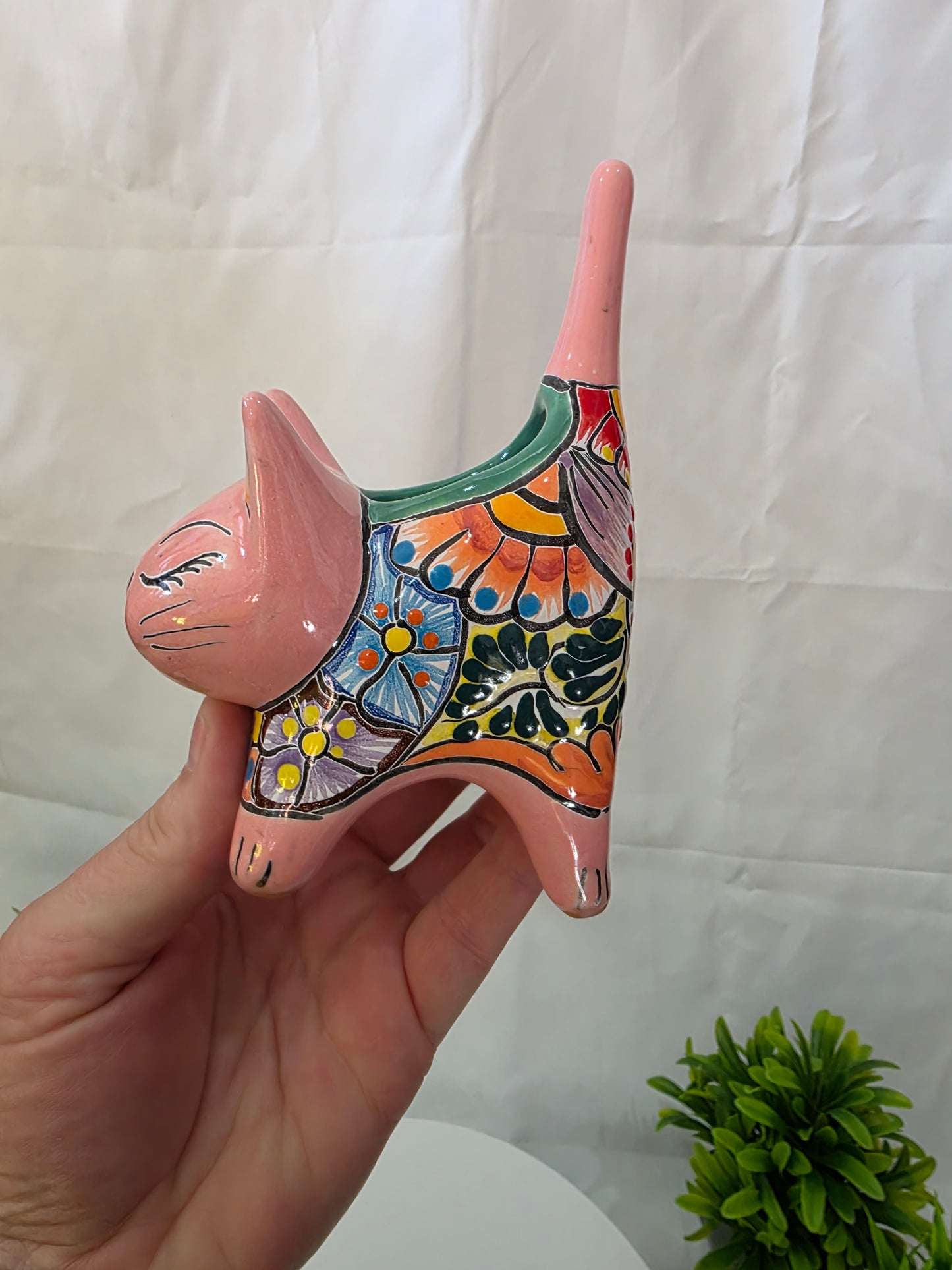 Hand holding a colorful ceramic cat planter against a white background