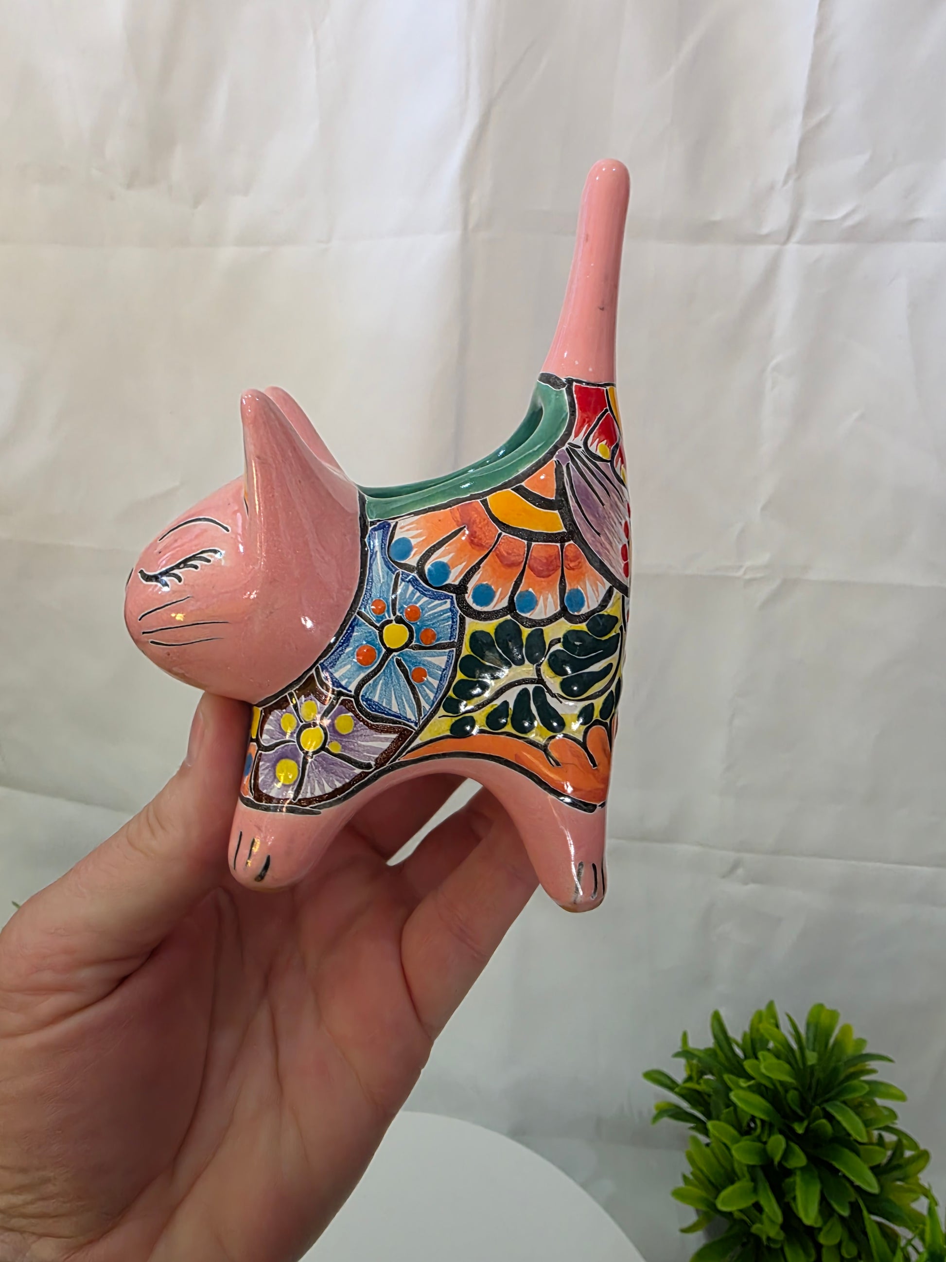 Hand holding a colorful ceramic cat planter against a white background