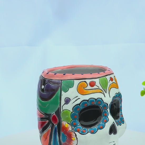 A colorful, hand-painted ceramic sugar skull planter with vibrant floral motifs rotating on a white background.
