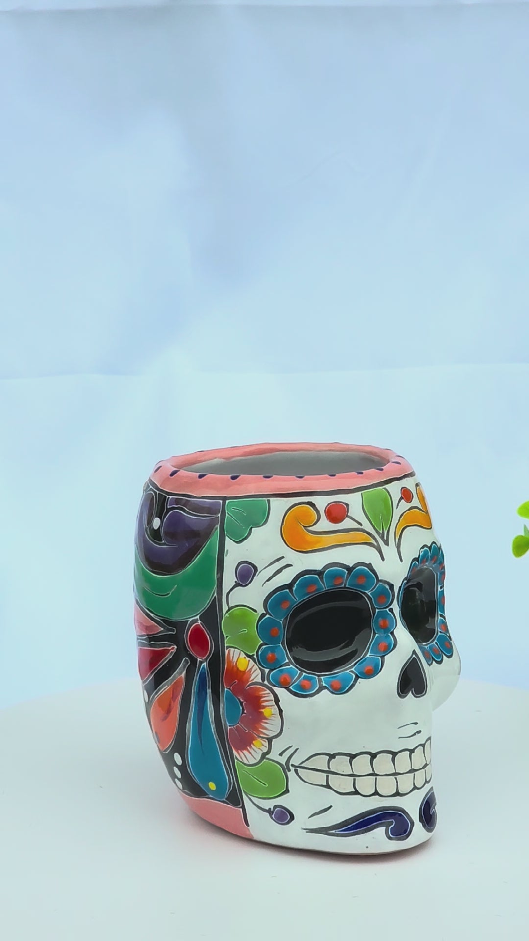 A colorful, hand-painted ceramic sugar skull planter with vibrant floral motifs rotating on a white background.