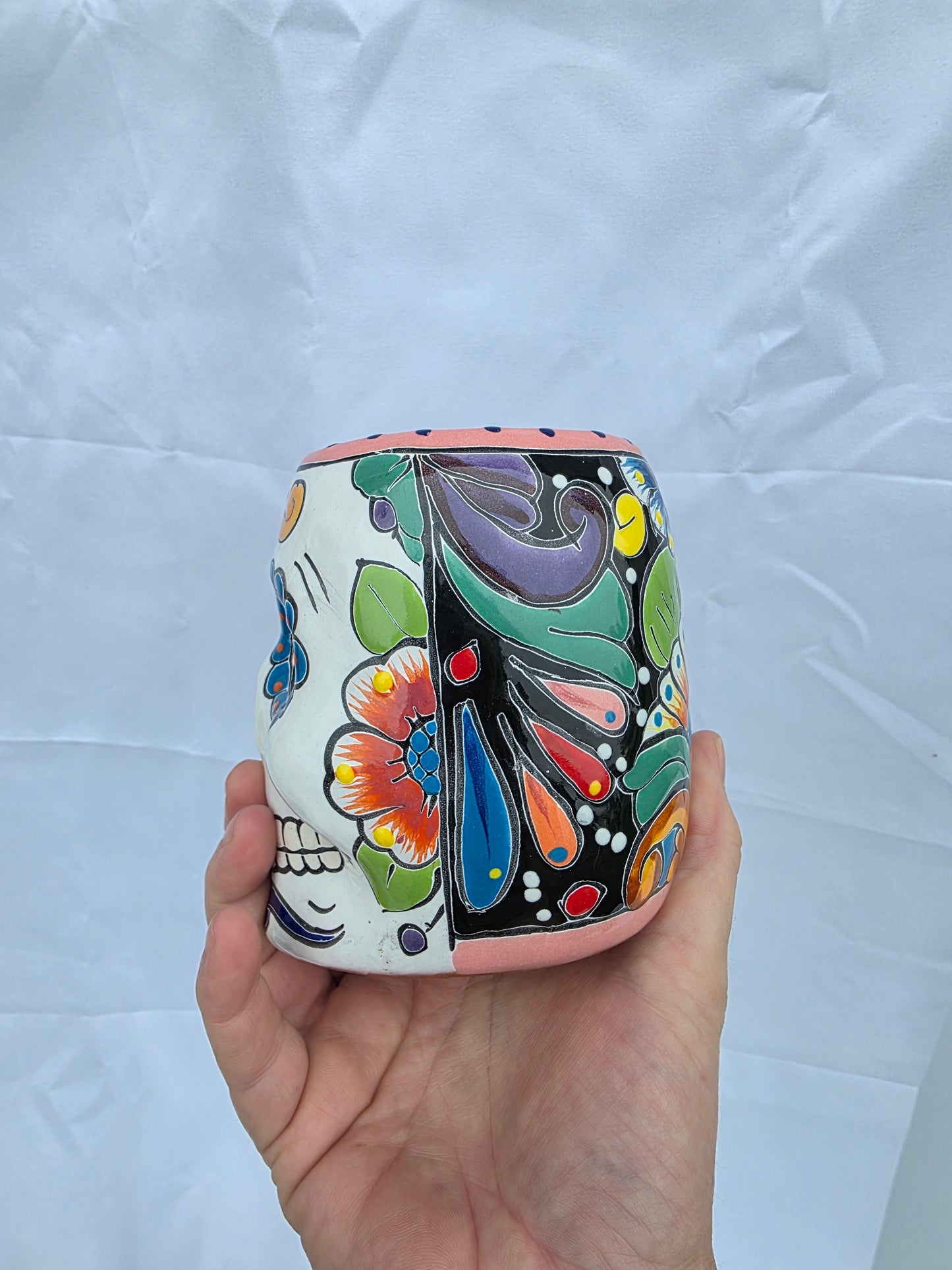 A hand holding a small cylindrical ceramic container decorated with colorful hand-painted floral and paisley patterns on a white background.
