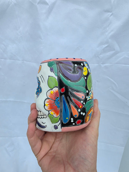 A hand holding a small cylindrical ceramic container decorated with colorful hand-painted floral and paisley patterns on a white background.