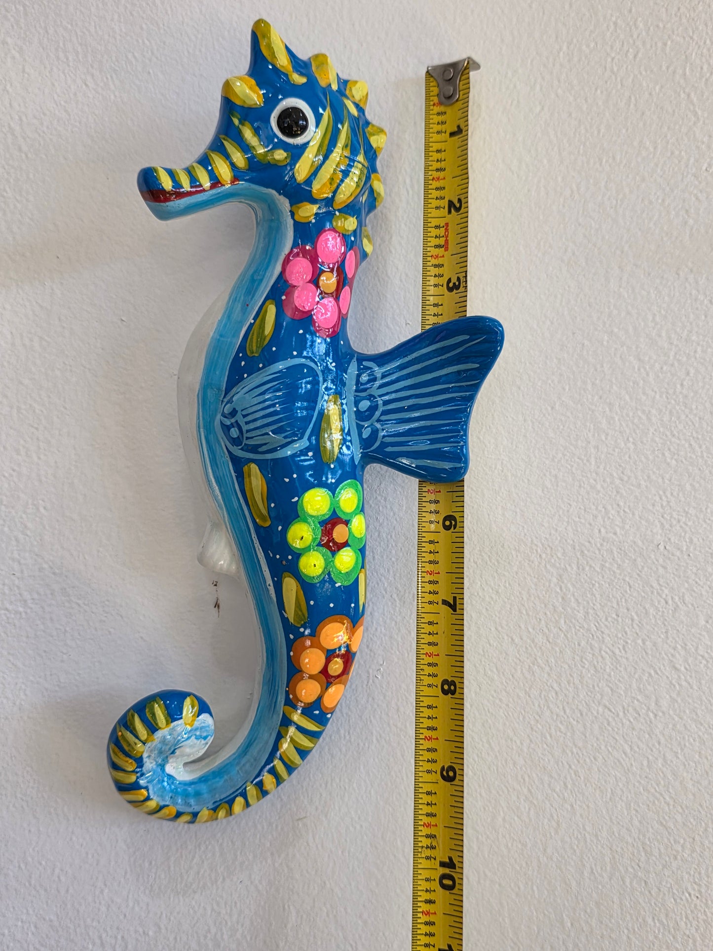 Colorful seahorse decoration next to a tape measure on a white wall